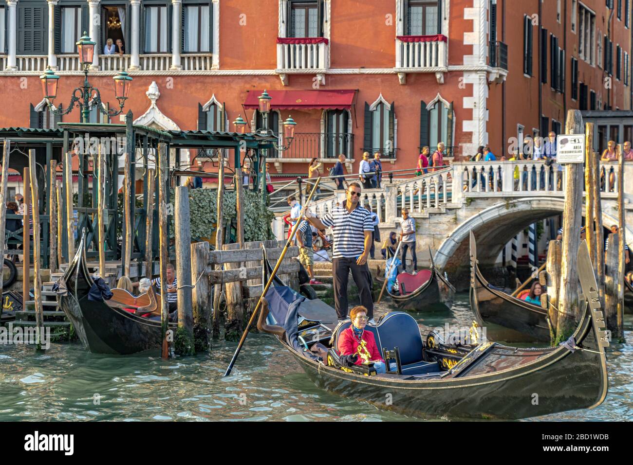 Two people watch from a balcony at The Hotel Danieli as Gondoliers take tourists for a gondola ride on The Grand Canal ,Venice Italy Stock Photo