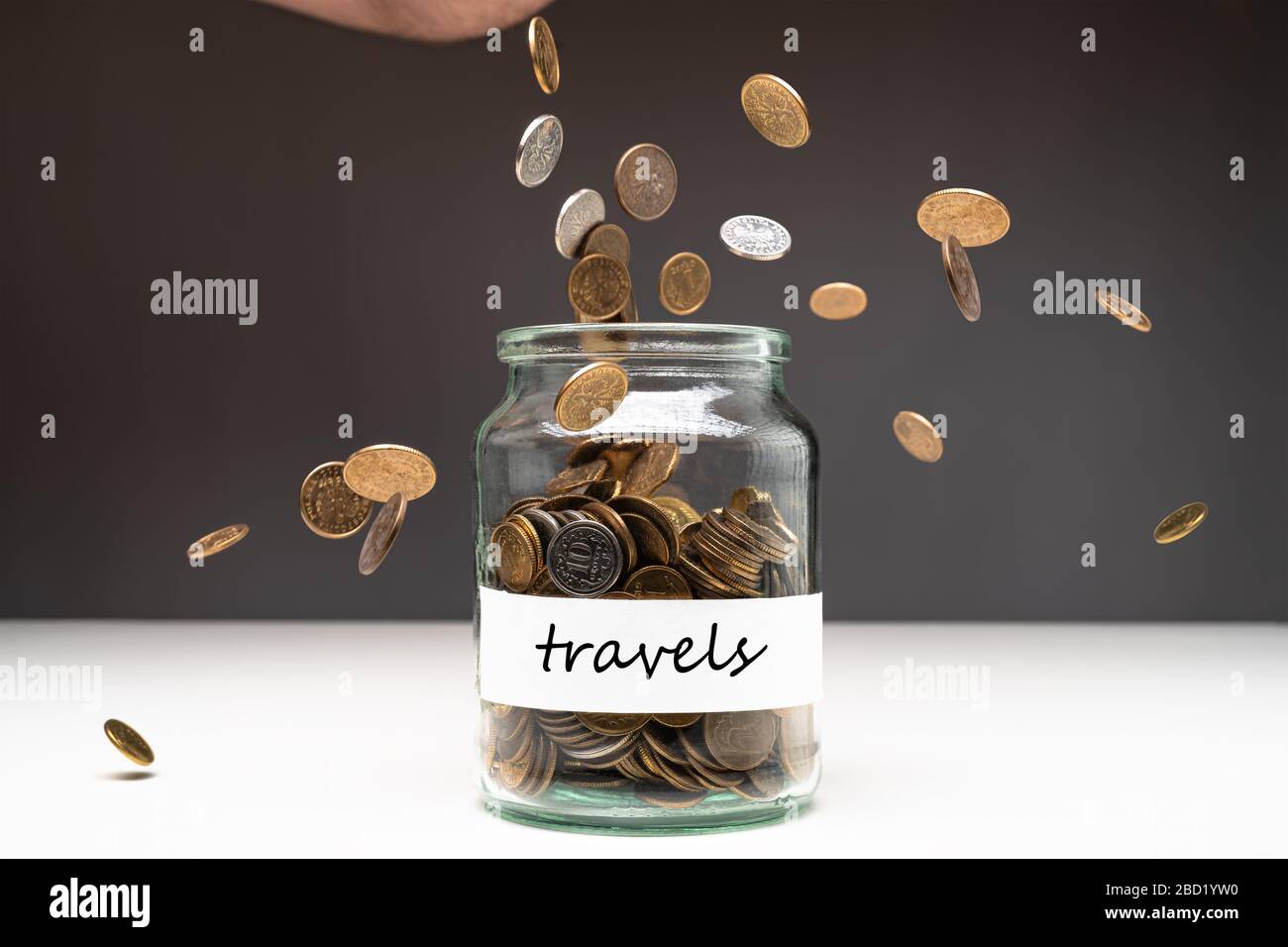 Coins in a jar with travels text on a white label. Money falling from the sky above. Savings abstract concept. Copy space. Stock Photo