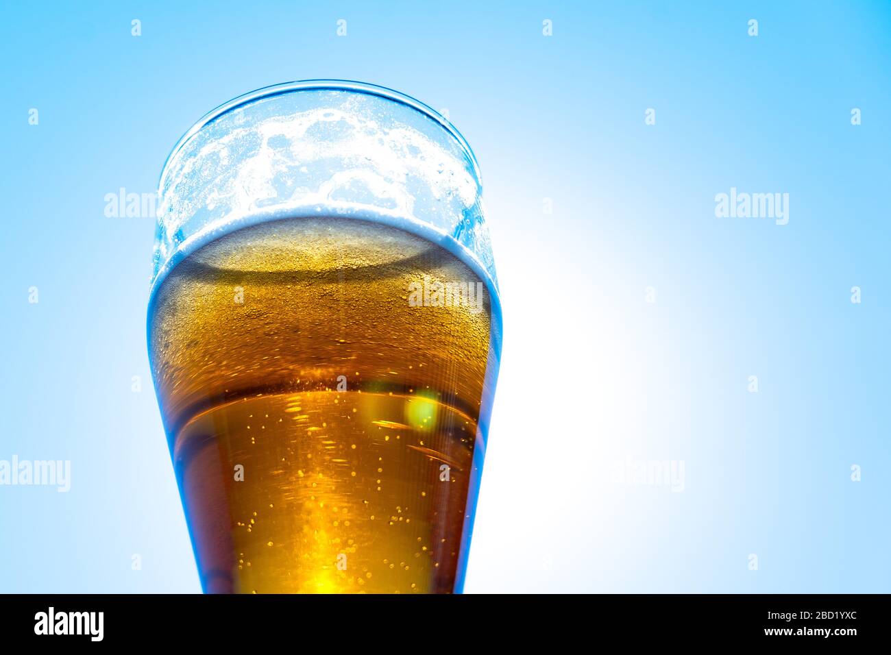 Light beer in a glass goblet on a background of blue sky. Beer foam on
