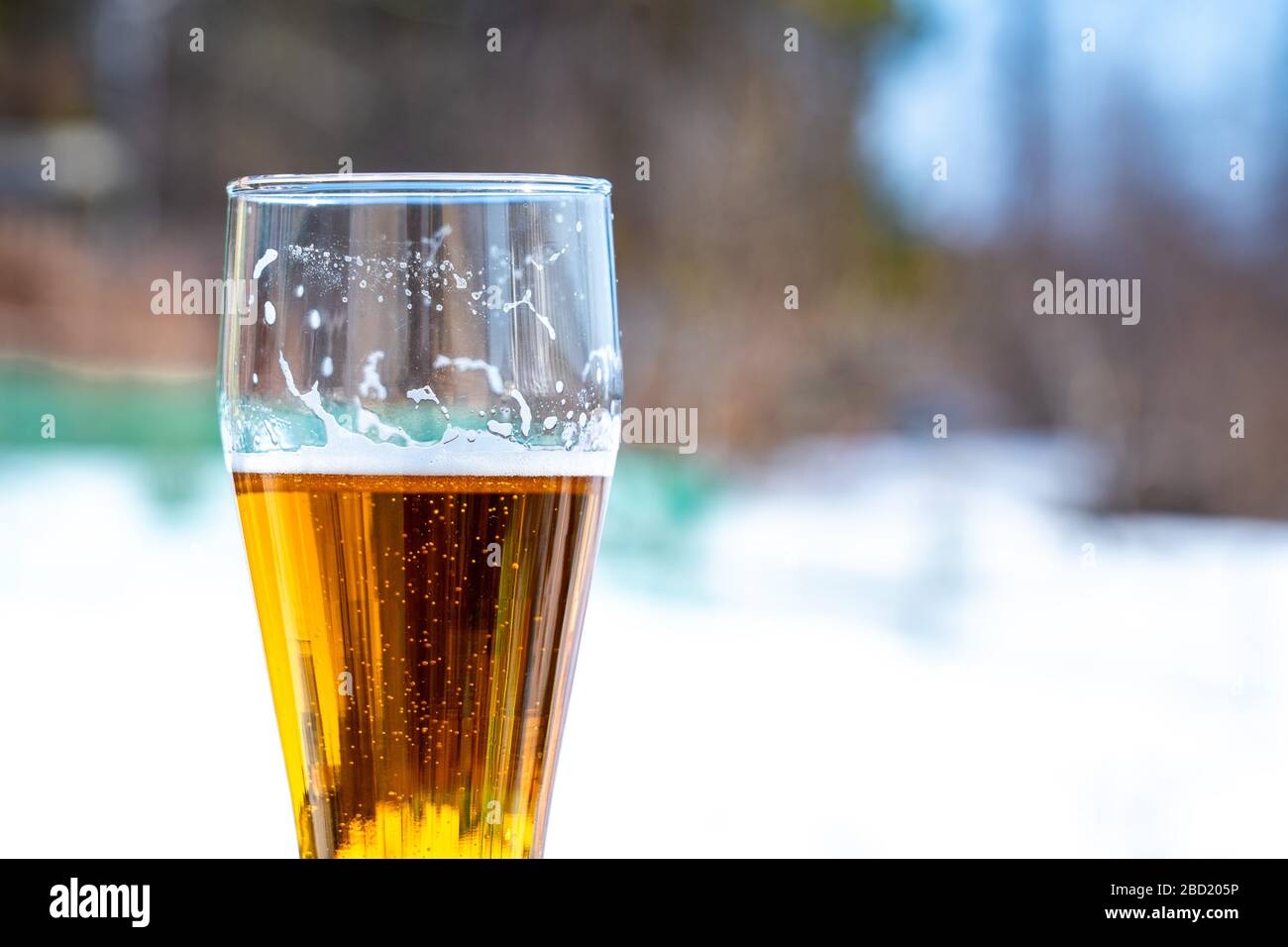 Light beer in a glass goblet on a picnic with snow background. Beer foam on the walls of a glass in the sunlight Stock Photo