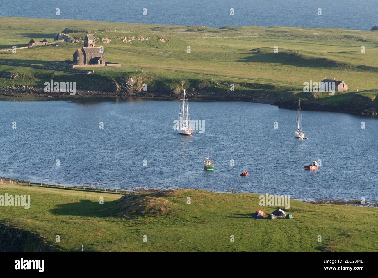 Sailing yachts and fishing boats in Canna harbour, looking across to the church on Sanday from Canna, Hebrides, Scotland Stock Photo