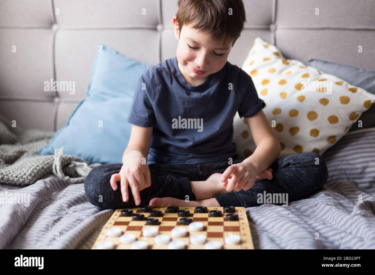Young kid hands playing checkers table game on bed. Stay at home Quarantine concept. Board game and kids leisure concept. Family time.  Stock Photo