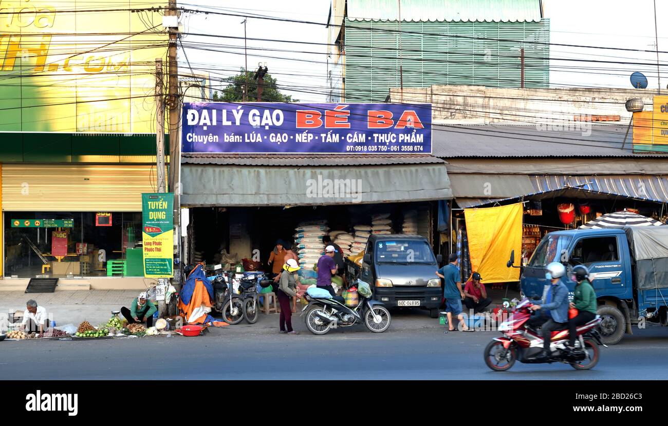 A street scene of a shop front, overloaded motorcycle, and seniors selling small collections of vegetables from the kerbside in Da Nang, Vietnam, Asia Stock Photo