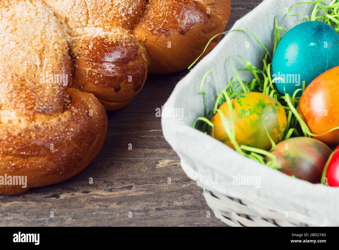 Easter wicker basket with colored eggs and Easter bread on grey wooden board. Stock Photo