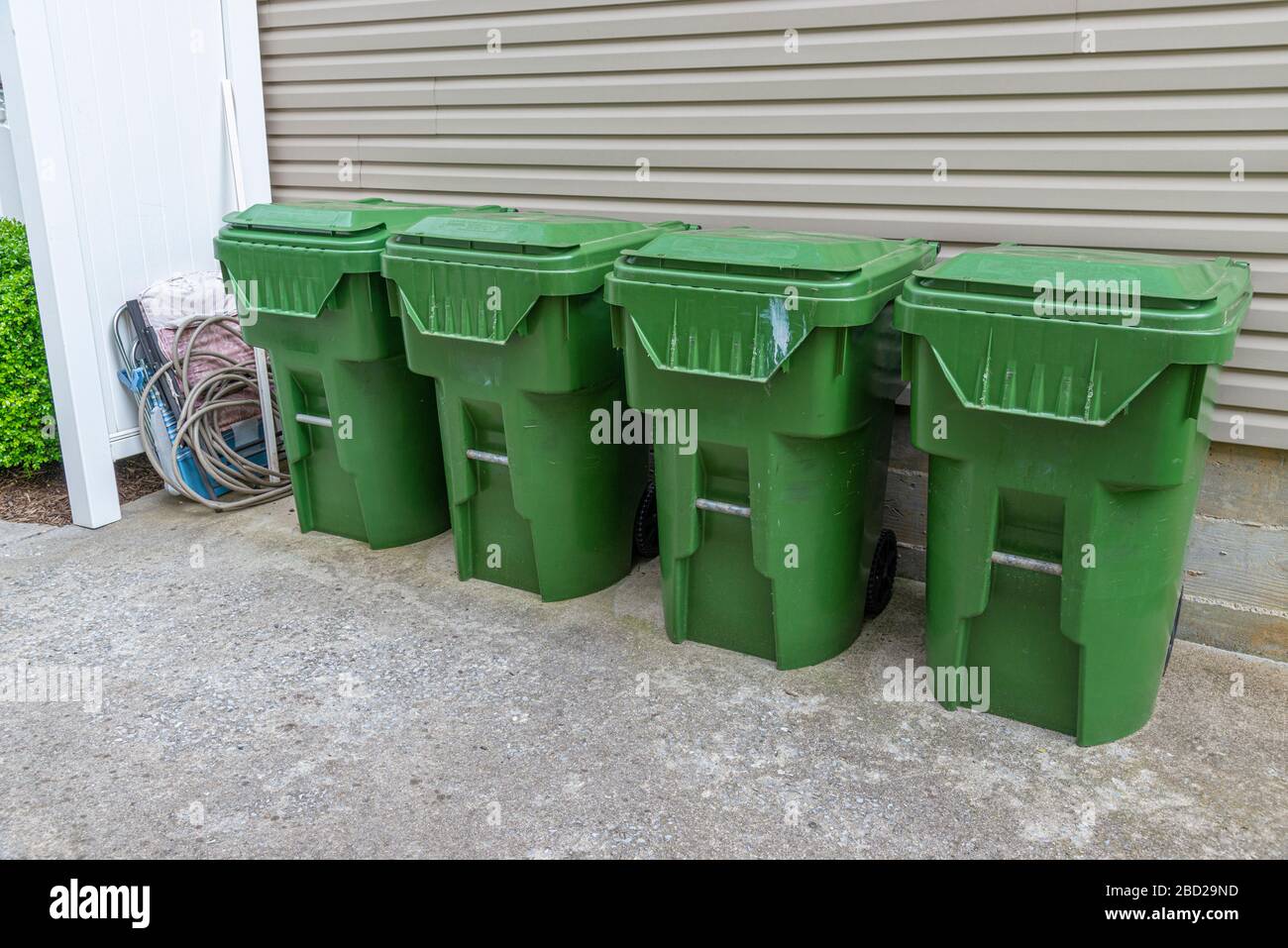 Horizontal shot of four green plastic trash cans lines up against the outside wall of a condominium. Stock Photo