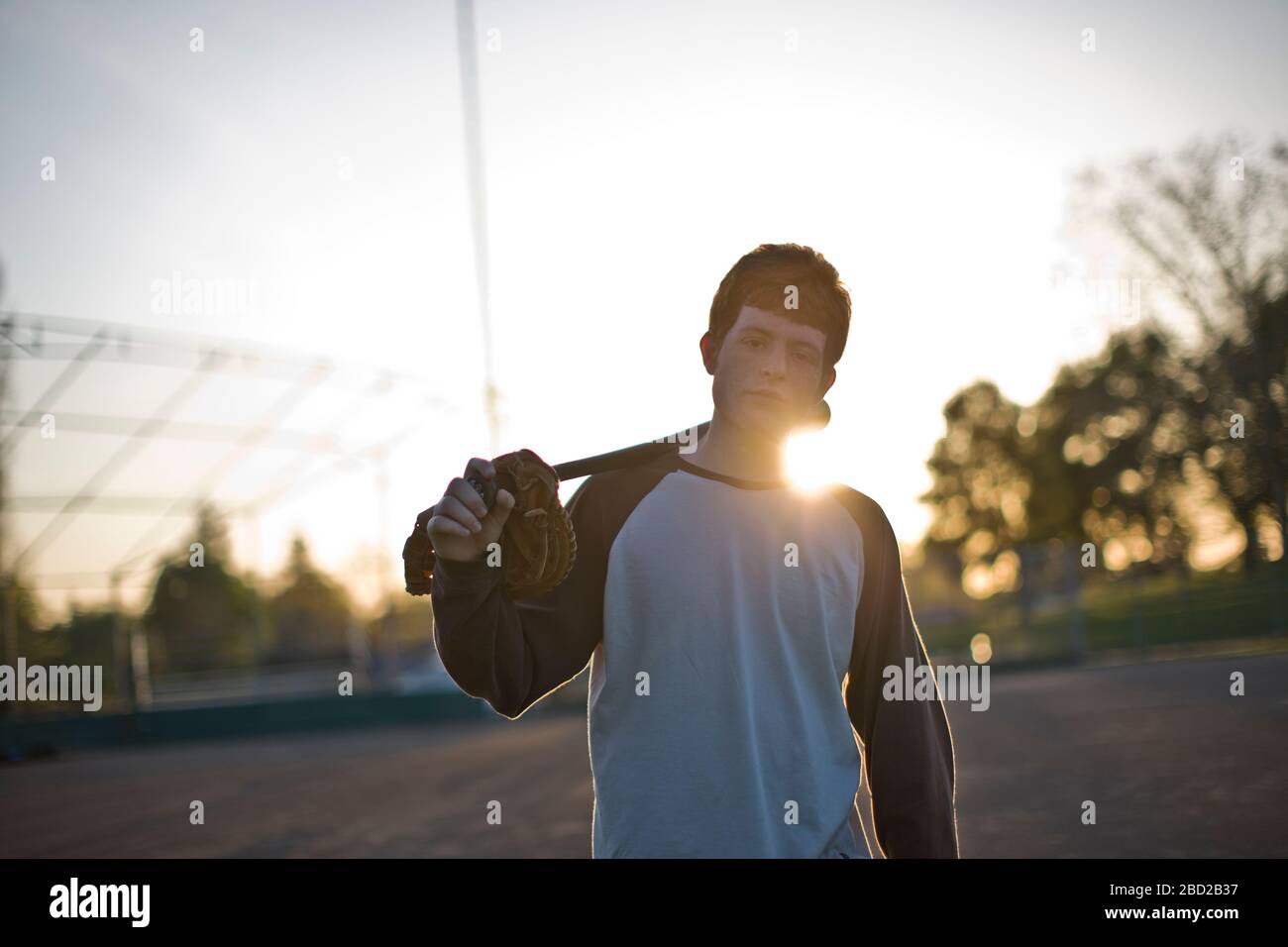 Portrait of a teenage boy carrying a baseball mitt and baseball bat
