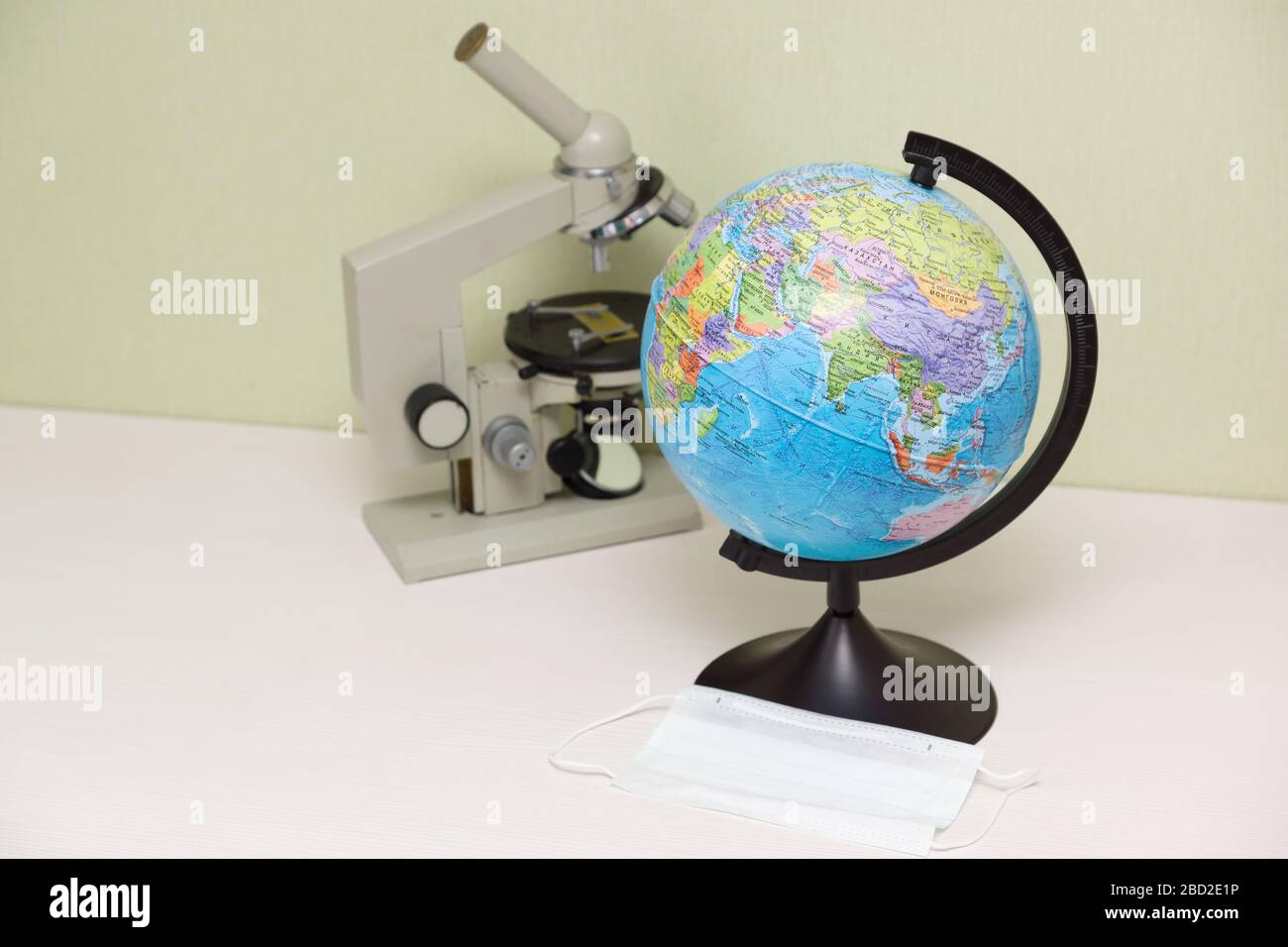 microscope and a globe with a protective mask stand on the table and symbolize the fight against Covid-19 Stock Photo