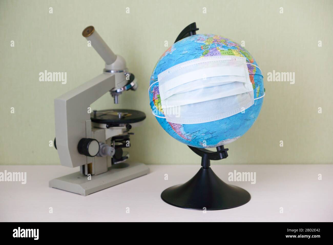 microscope and a globe with a protective mask stand on the table and symbolize the fight against Covid-19 Stock Photo