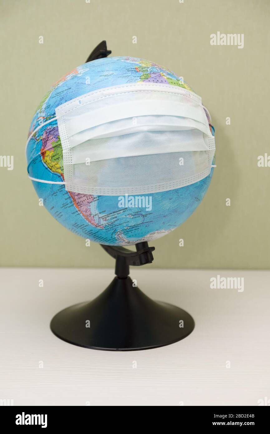 globe with a protective mask stands on the table and symbolizes the fight against Covid-19 Stock Photo