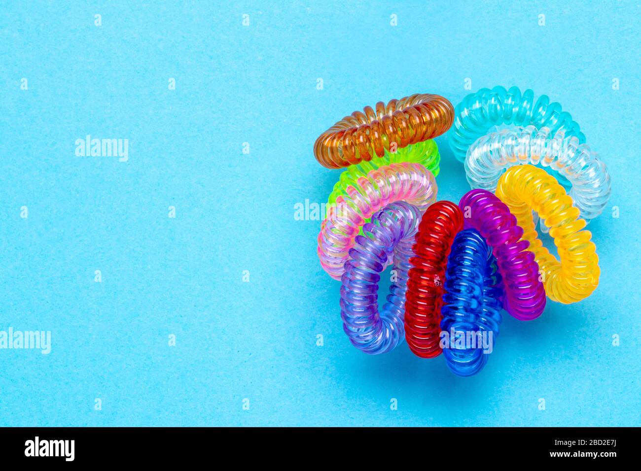 Close-up of multicolored elastic spiral scrunchies or hair bands for women hairstyling over blue background. Hair care tools from hairdresser and beau Stock Photo
