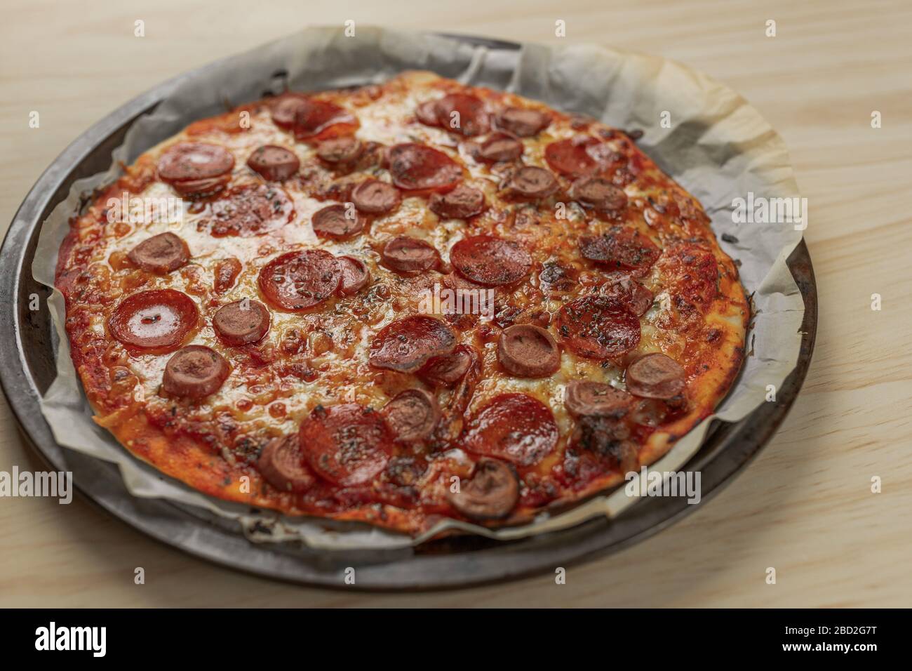 Overhead photography of a homemade pepperoni and sausage pizza on metal tray with a black napkin in a wooden table Stock Photo