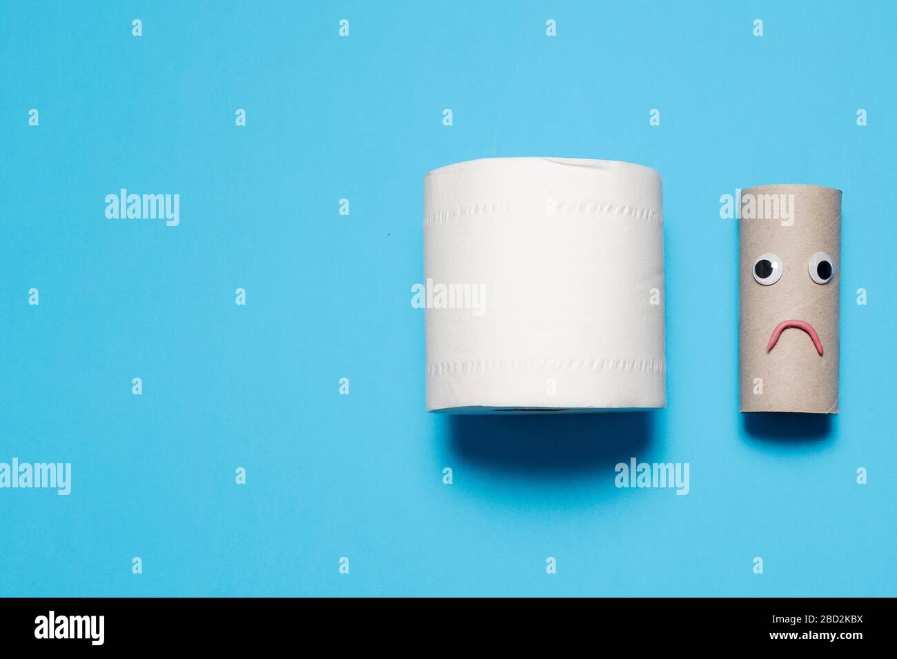 Full roll of toilet paper next to a sad and frowning empty roll with googly eyes and mouth on a blue background with copy space and room for text Stock Photo