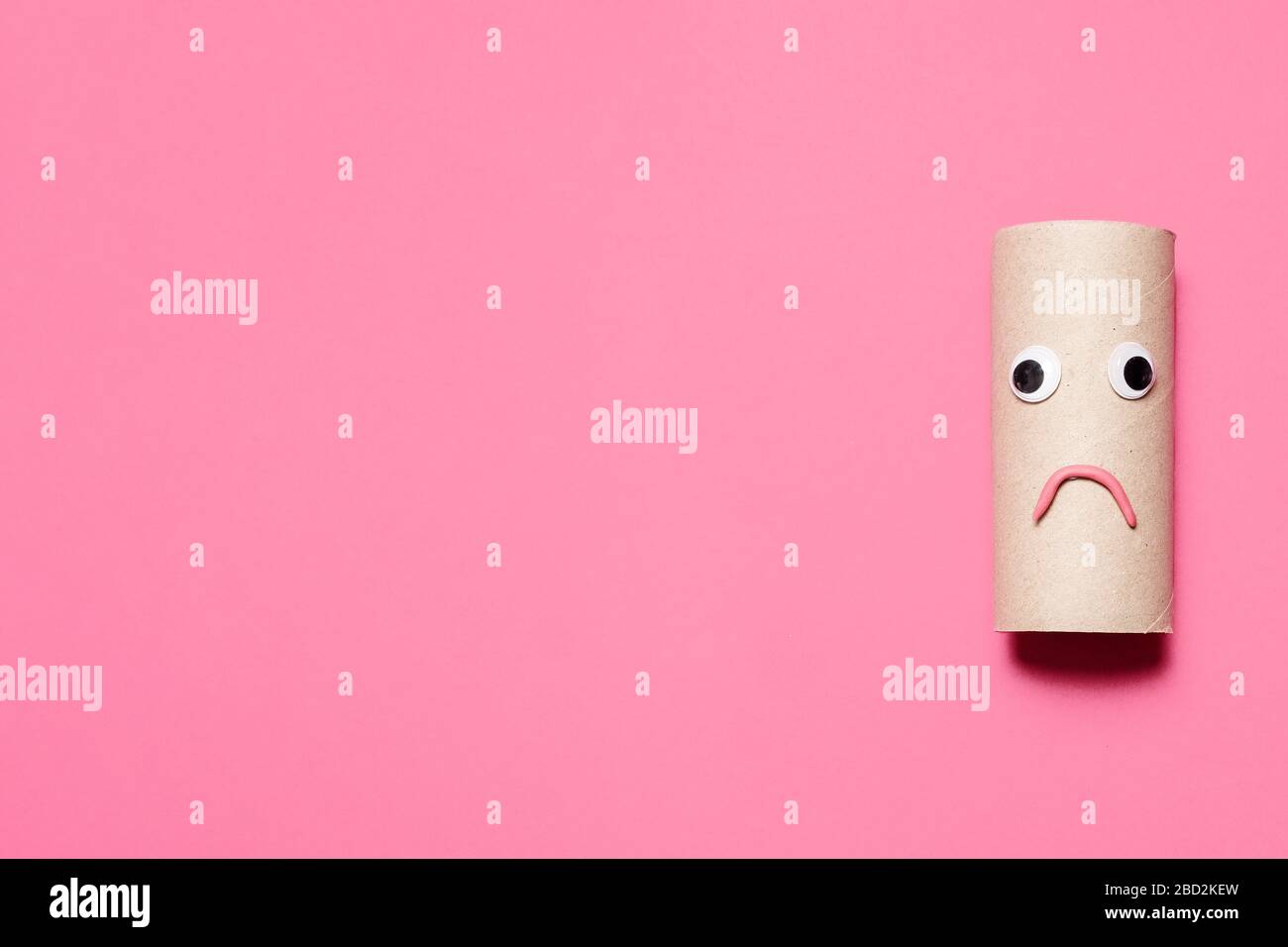Sad and frowning empty roll of toilet paper with googly eyes and mouth on a pink background with copy space and room for text. Stock Photo