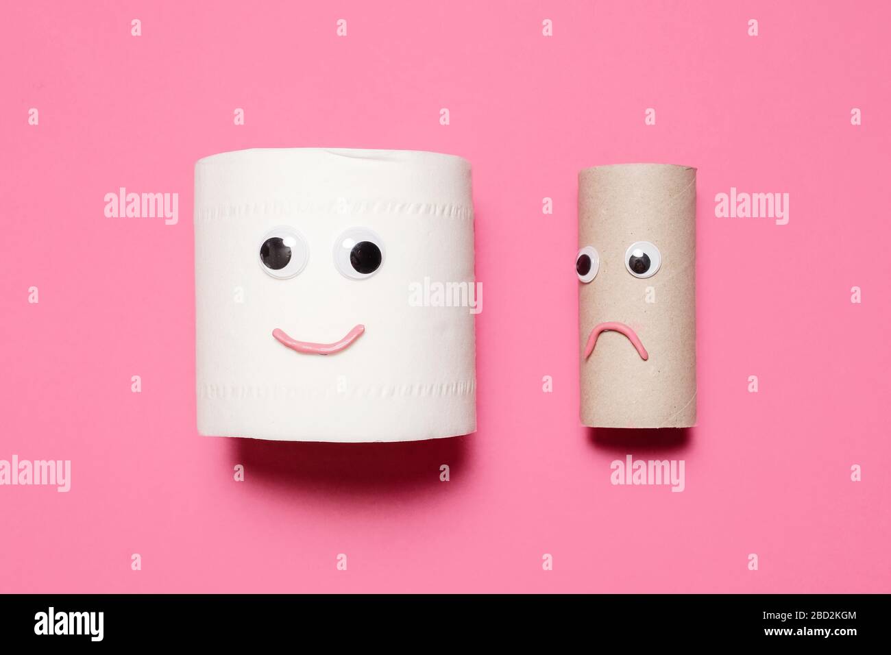 Happy and smiling full roll of toilet paper next to sad empty roll with googly eyes and mouth on a pink background with copy space and room for text. Stock Photo