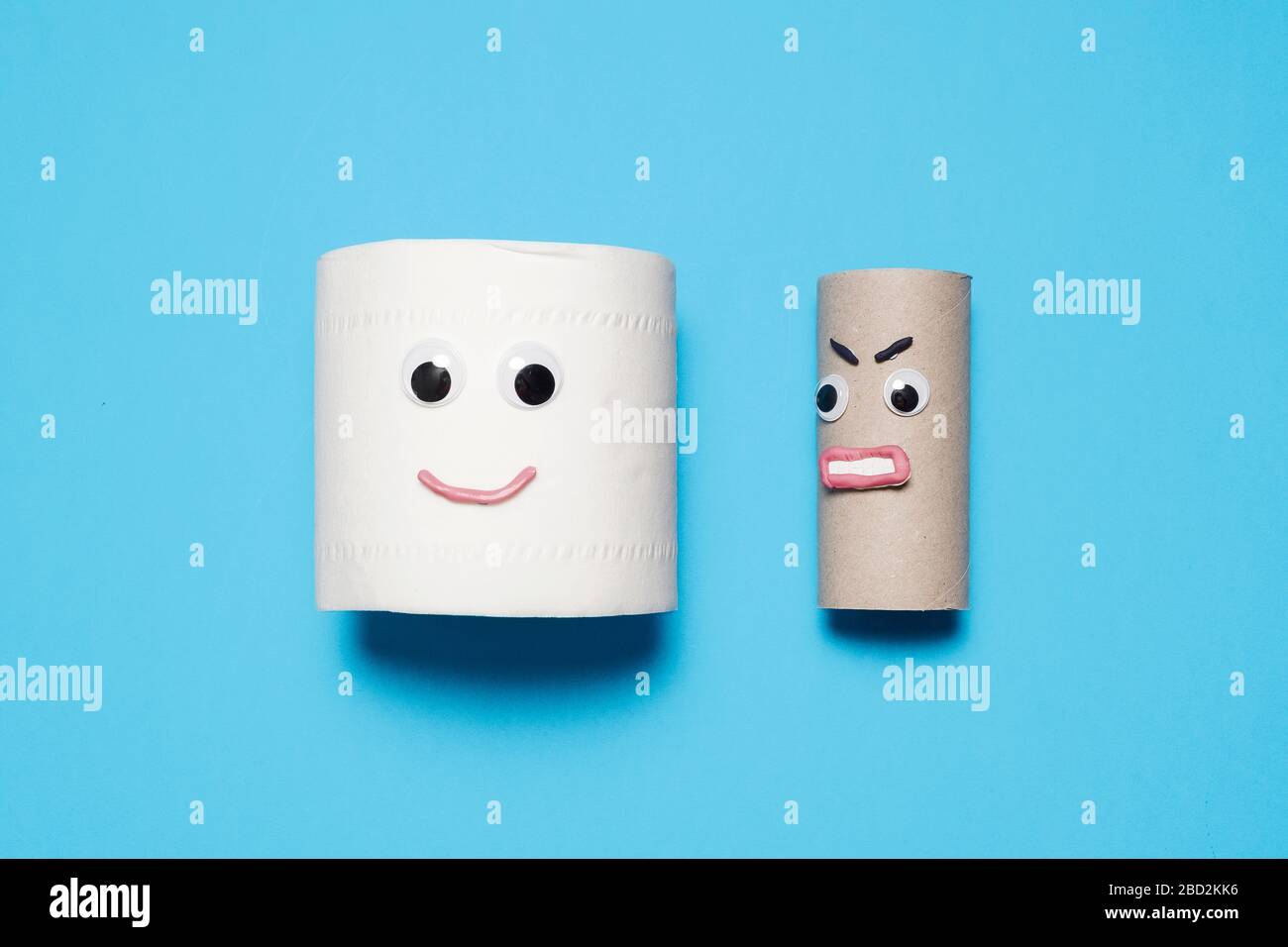 Happy smiling full roll of toilet paper next to angry empty roll with googly eyes and mouth on a blue background with copy space and room for text Stock Photo