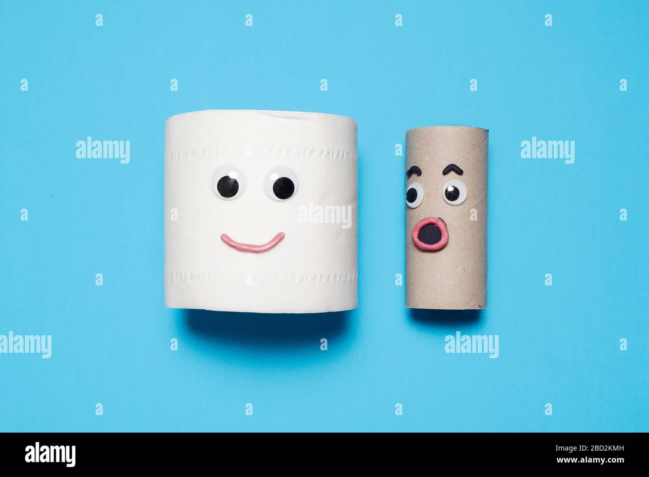 Happy smiling full roll of toilet paper next to surprised empty roll with googly eyes and mouth on a blue background with copy space and room for text Stock Photo