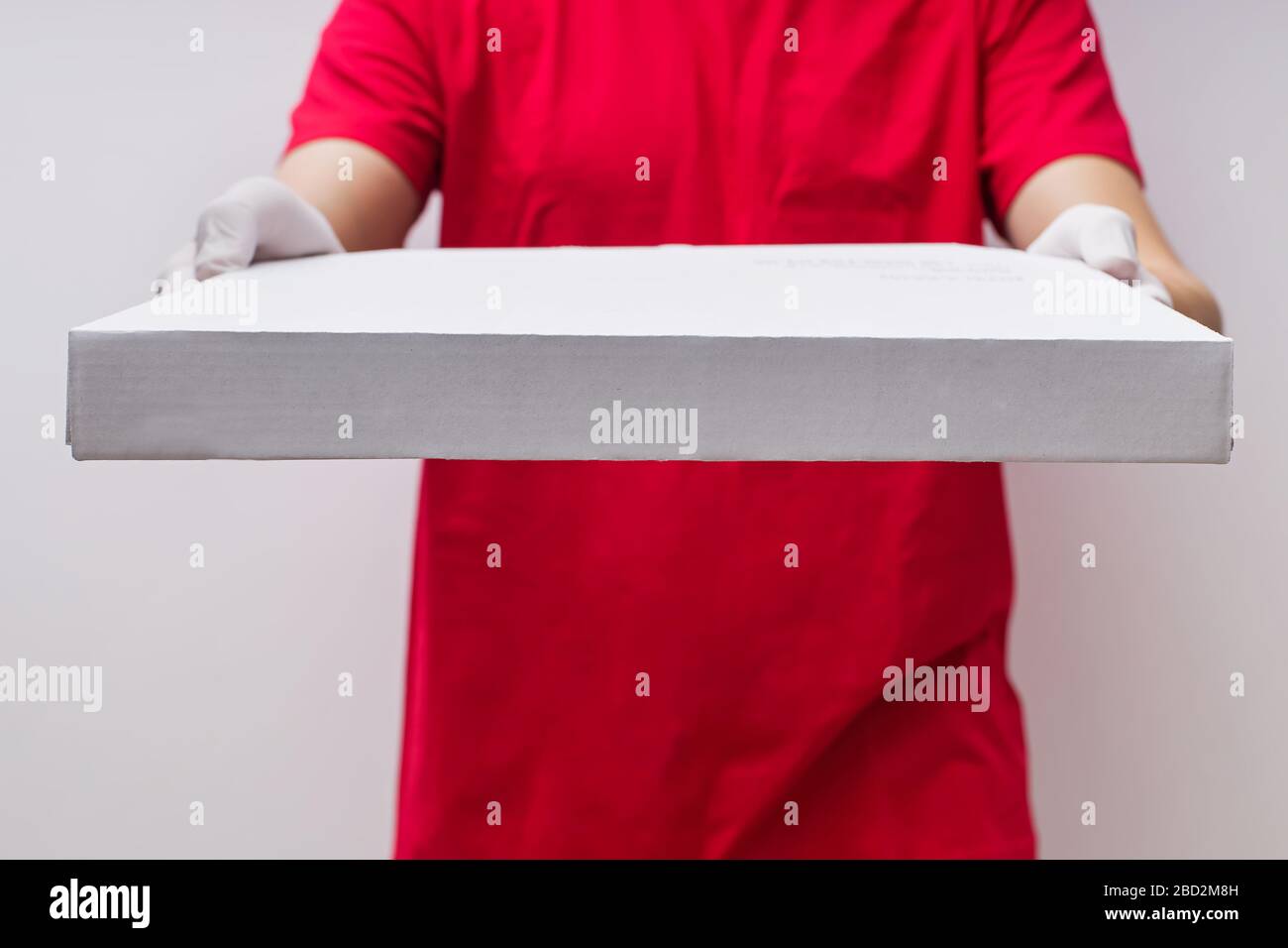 Man from delivery service in red t-shirt and protective gloves giving pizza box close-up Stock Photo