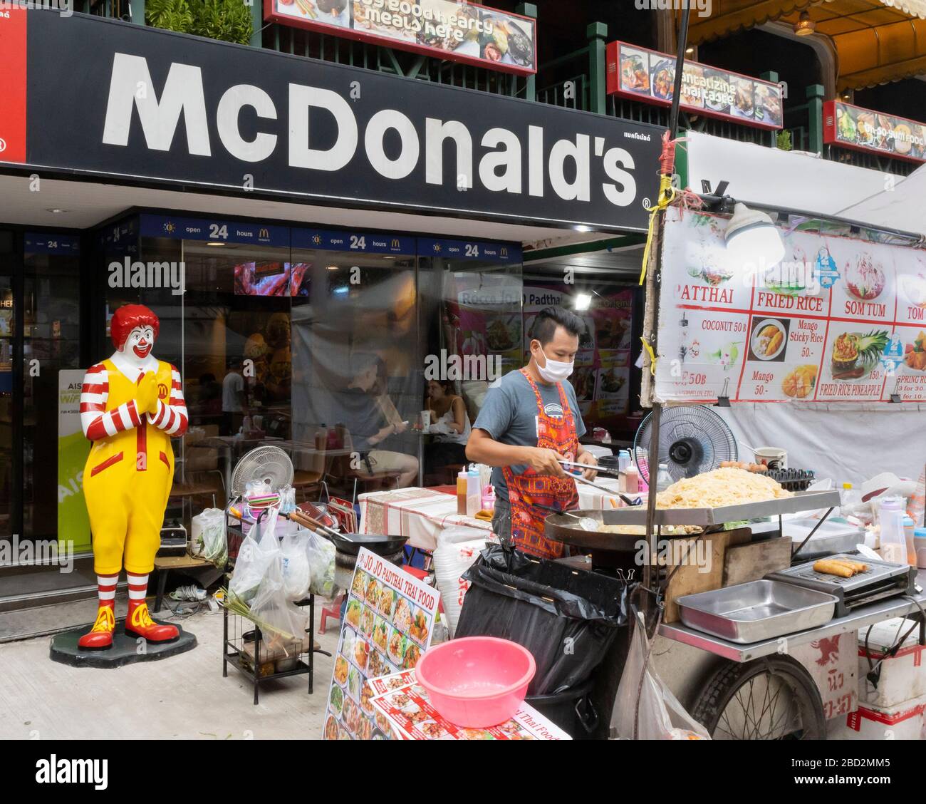 Bangkok, Thailand - February 27th, 2020: A traditional thai street food vendor in front of a local McDonald's fast food branch. Stock Photo
