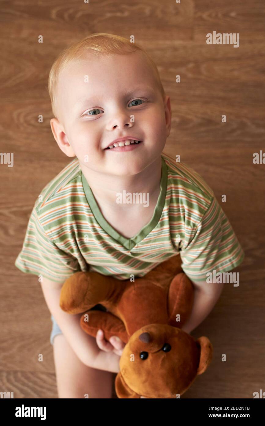 A happy smiling boy sits on the floor and holds a teddy bear Stock ...