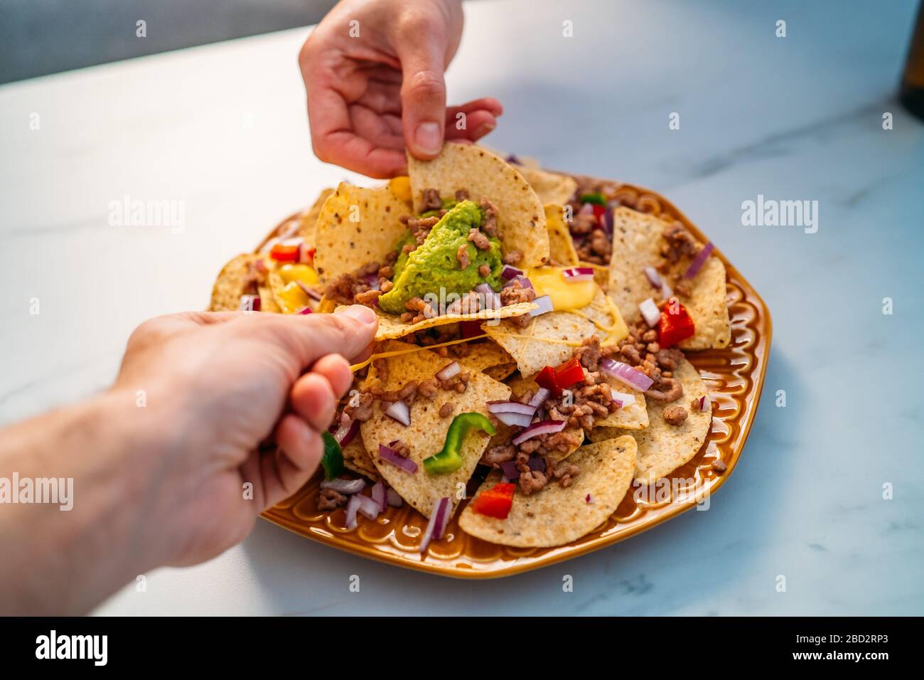 People hands dipping Yellow corn nacho chips garnished with ground beef