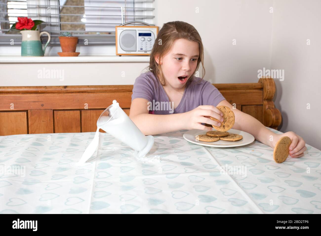 Young girl spilling a glass of milk over the kitchen table Stock Photo