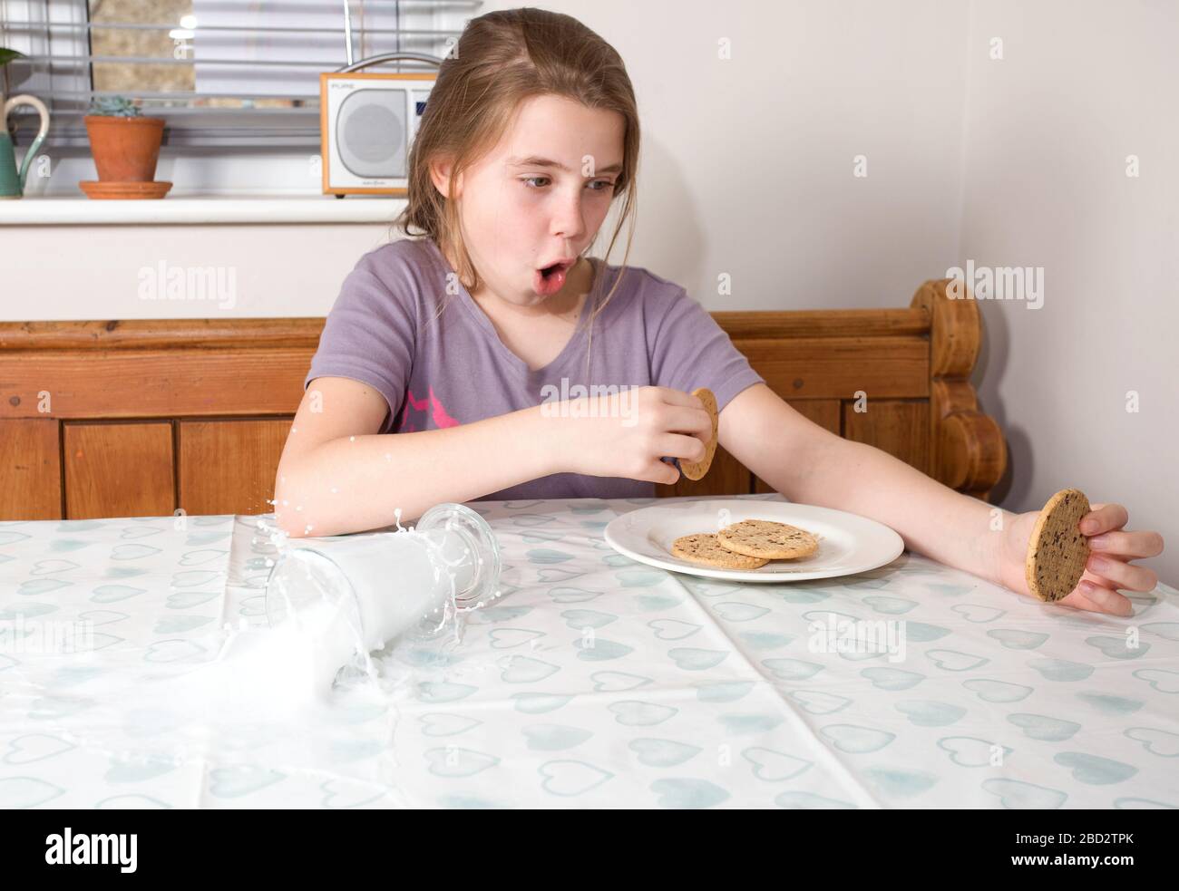 Young girl spilling a glass of milk over the kitchen table Stock Photo