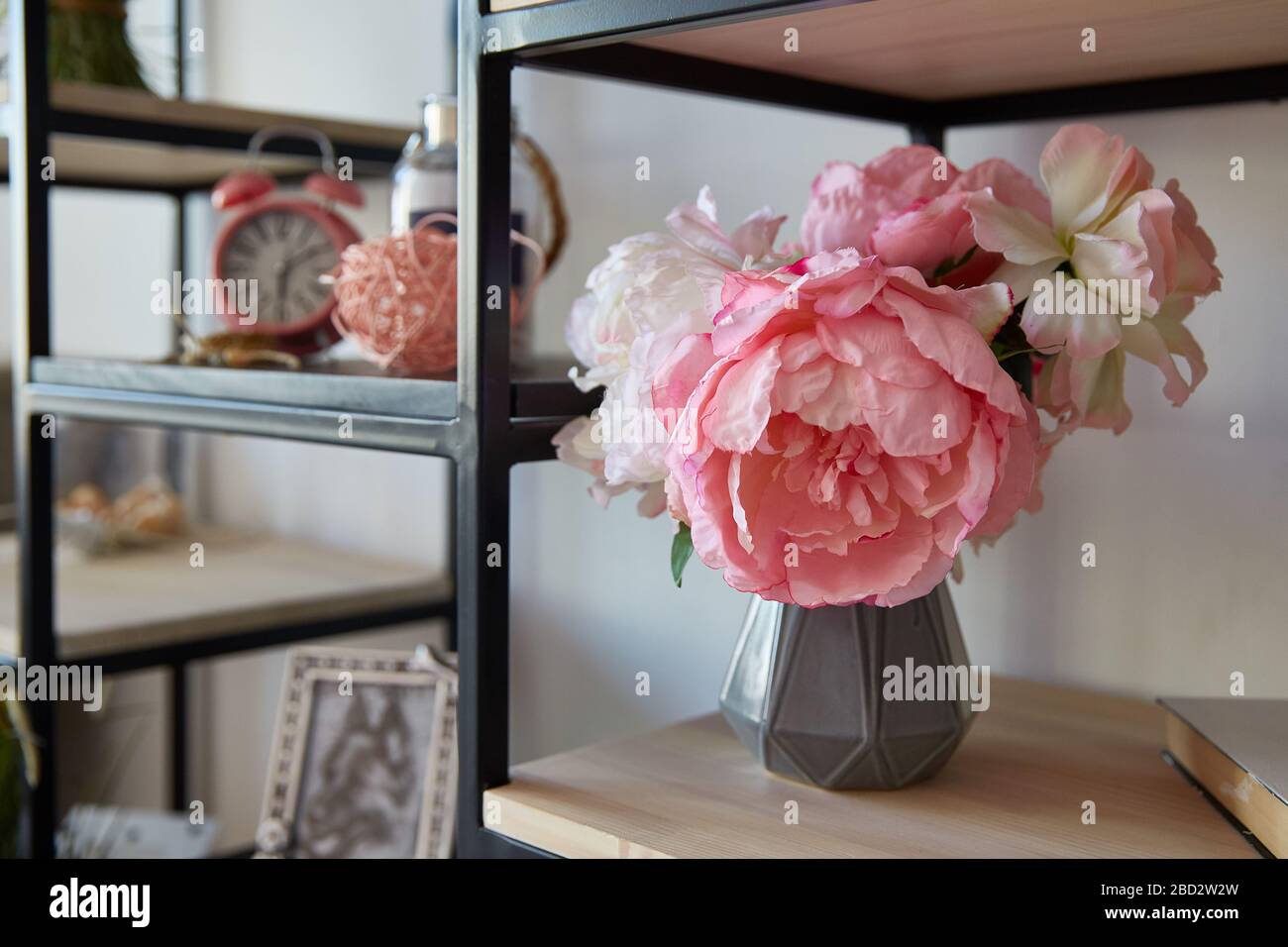 a vase with pink flowers with stands alarm clock on a shelf in the room ...