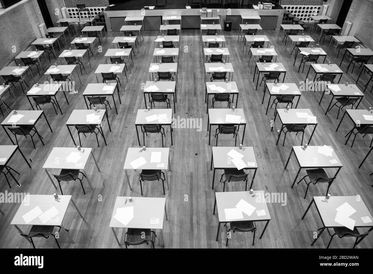 rows of empty tables and chairs in exam room at highschool in black and white Stock Photo