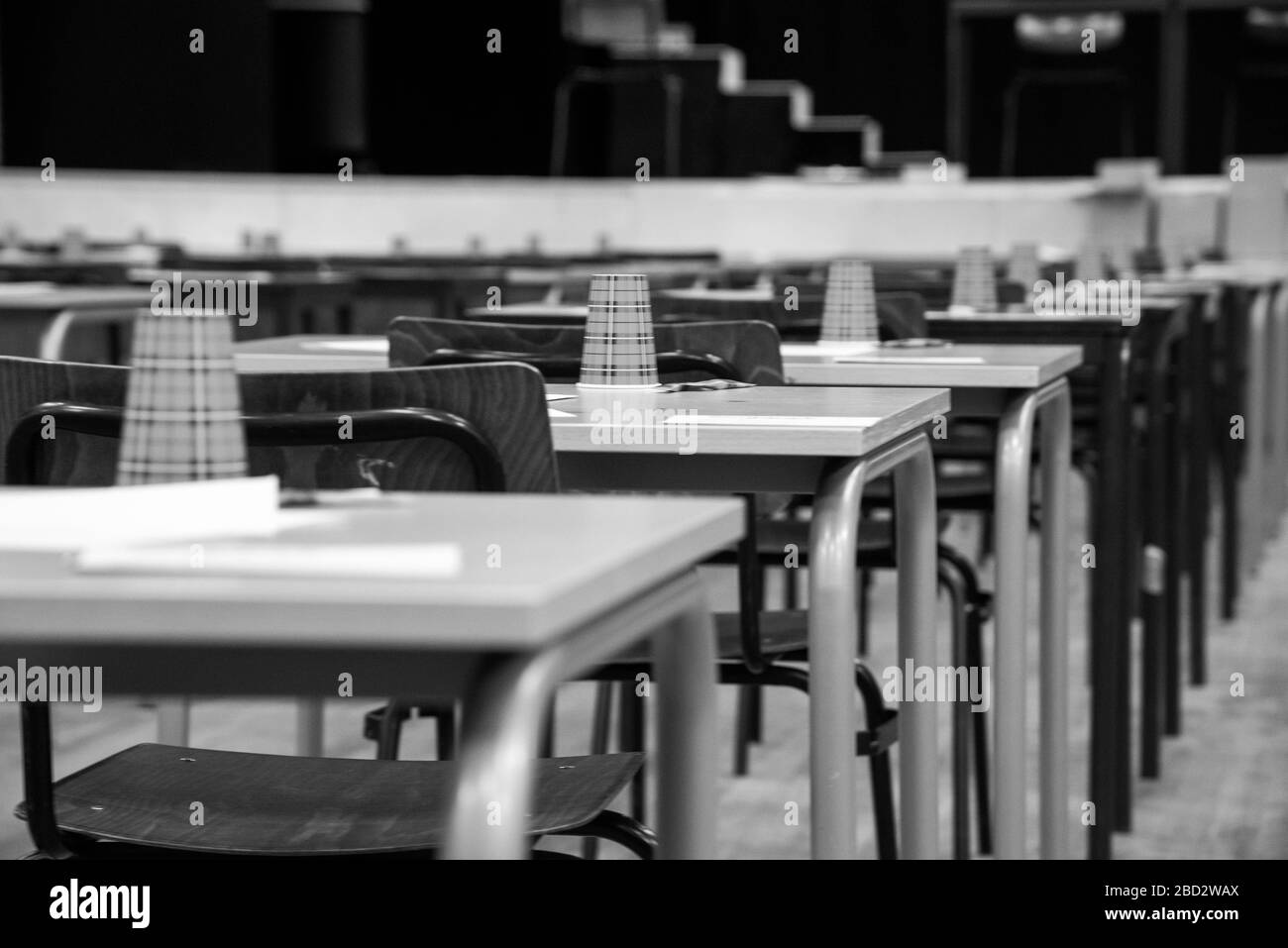 rows of empty tables and chairs in exam room at highschool in black and white Stock Photo