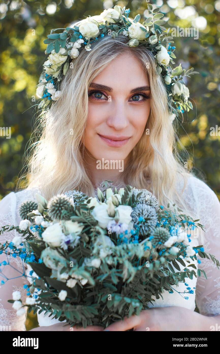 Beautiful blonde young bride portrait with flower bouquet and wreath on ...