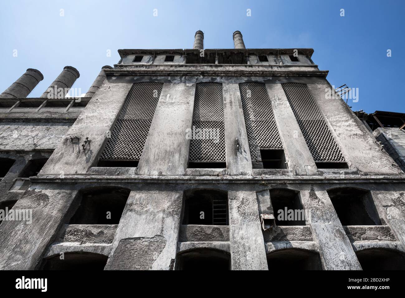 Symmetrical wide angle view from below of the facade of an old concrete factory in northern Italy, against a solid blue sky Stock Photo