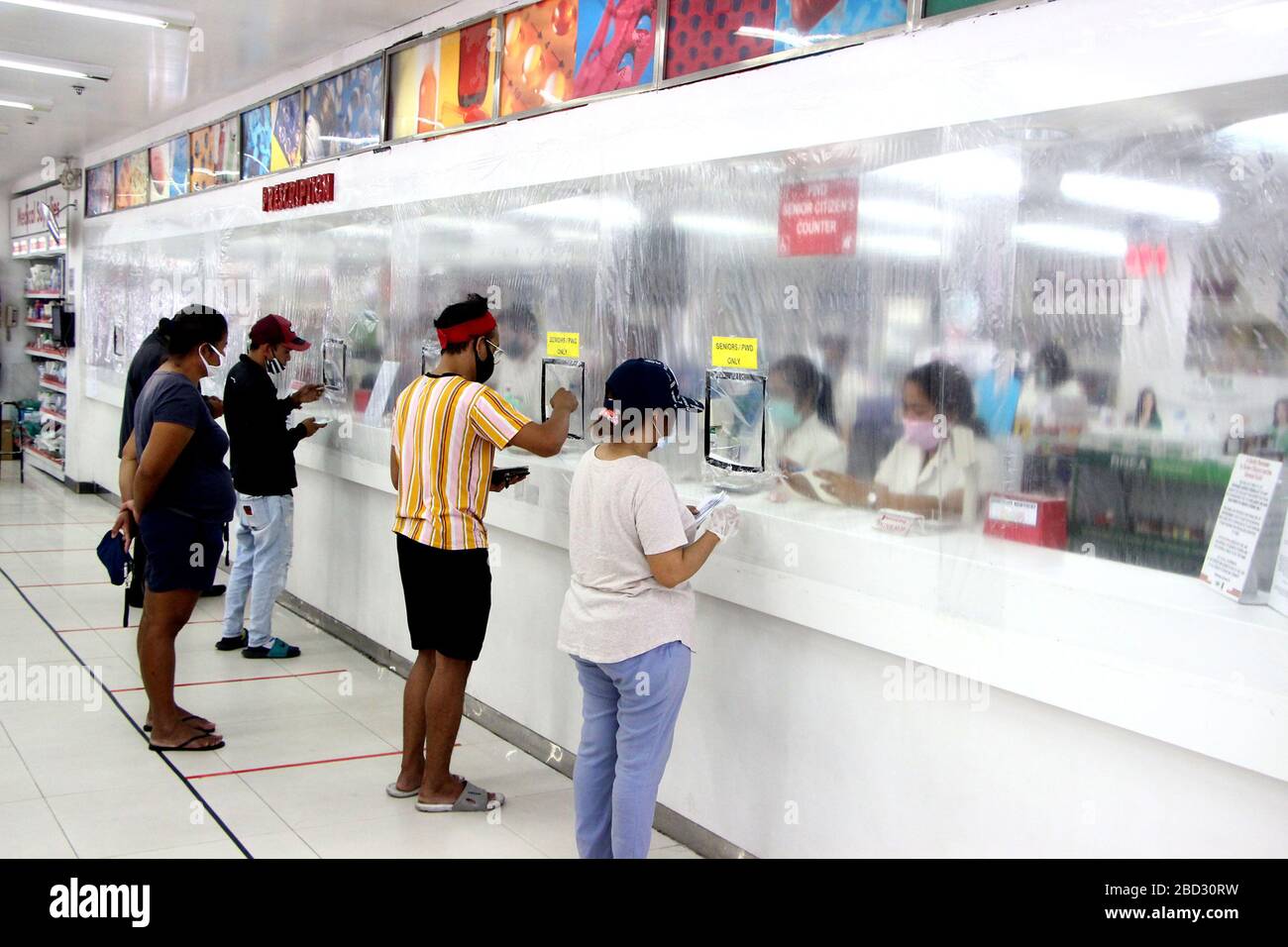 Customer's in line with the social distance rules inside of Mercury Drugs in Cainta province of Rizal on April 6, 2020. The managements cover the counters with plastics to limits the contacts of costumers and store employees to protect their self for possible infection from COVIS - 19. Local government of Rizal province declared a total lock down for not Rizal province to control the spread of the virus.Customer's in line with the social distance rules inside of Mercury Drugs in Cainta province of Rizal on April 6, 2020. The managements cover the counters with plastics to limits the contacts o Stock Photo