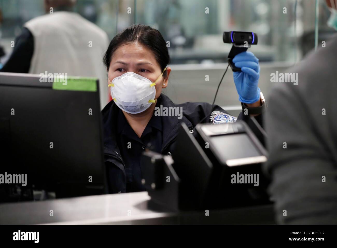 An officer with U.S. Customs and Border Protection Office of Field Operations takes a photo of an arriving international traveler at Dulles International Airport in Dulles, Va., March 18, 2020. In response to the coronavirus pandemic, CBP officers have donned personal protective equipment (PPE) as they work on the frontlines of the crisis. CBP Photo by Glenn Fawcett Stock Photo