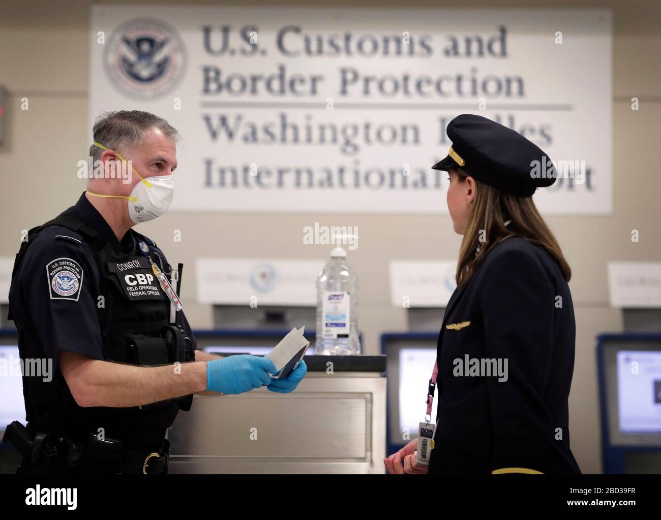 An officer with U.S. Customs and Border Protection Office of Field Operations reviews travel the documents of an arriving international airline pilot at Dulles International Airport in Dulles, Va., March 18, 2020. In response to the coronavirus pandemic, CBP officers have donned personal protective equipment (PPE) as they work on the frontlines of the crisis. CBP Photo by Glenn Fawcett Stock Photo