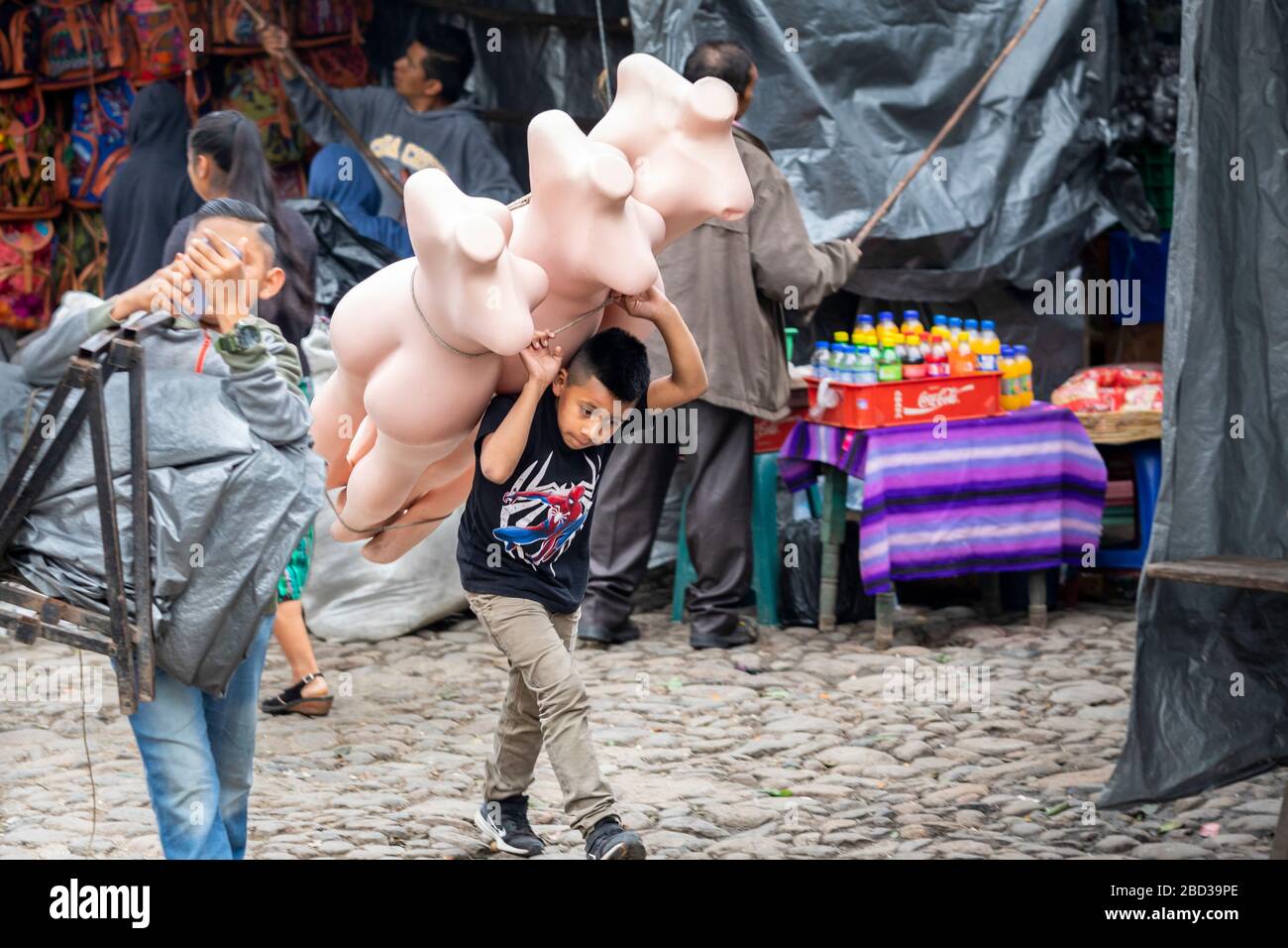 Young boy carries mannequins to his family's stall in the market of Chichicastenango, Guatemala. Stock Photo