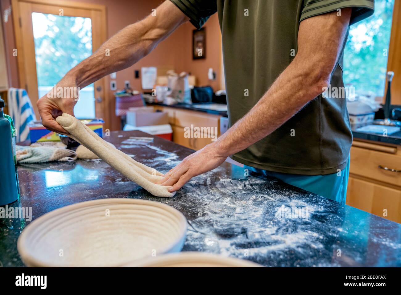 Man stretching sourdough bread dough in messy kitchen Stock Photo