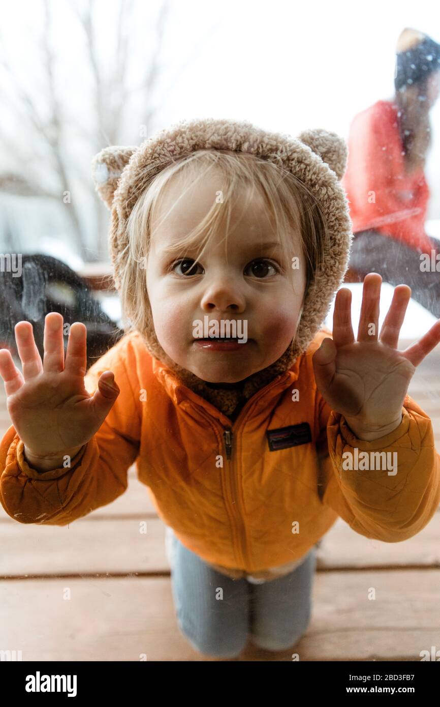 young blonde kid pushes face and hands against glass during quarantine Stock Photo