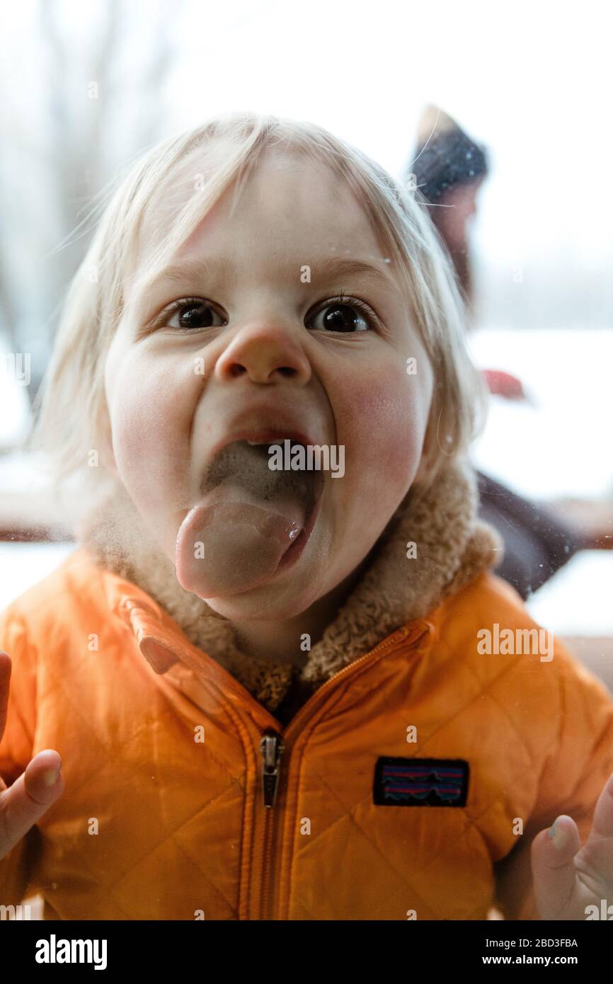 3 year old toddler girl smashes her tongue and face against window Stock Photo