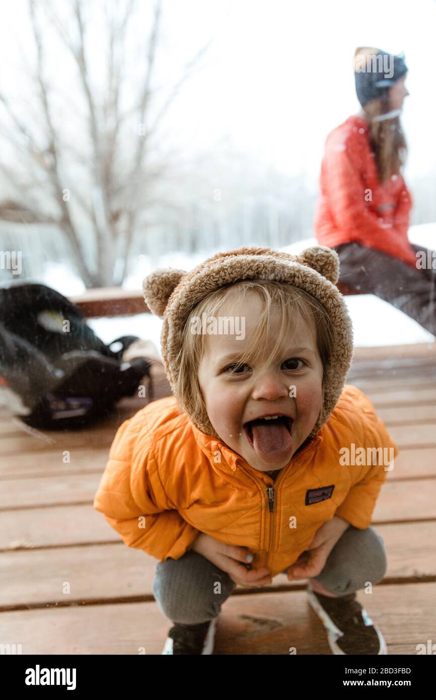 three year old smiling girl looks through window with tongue out Stock Photo