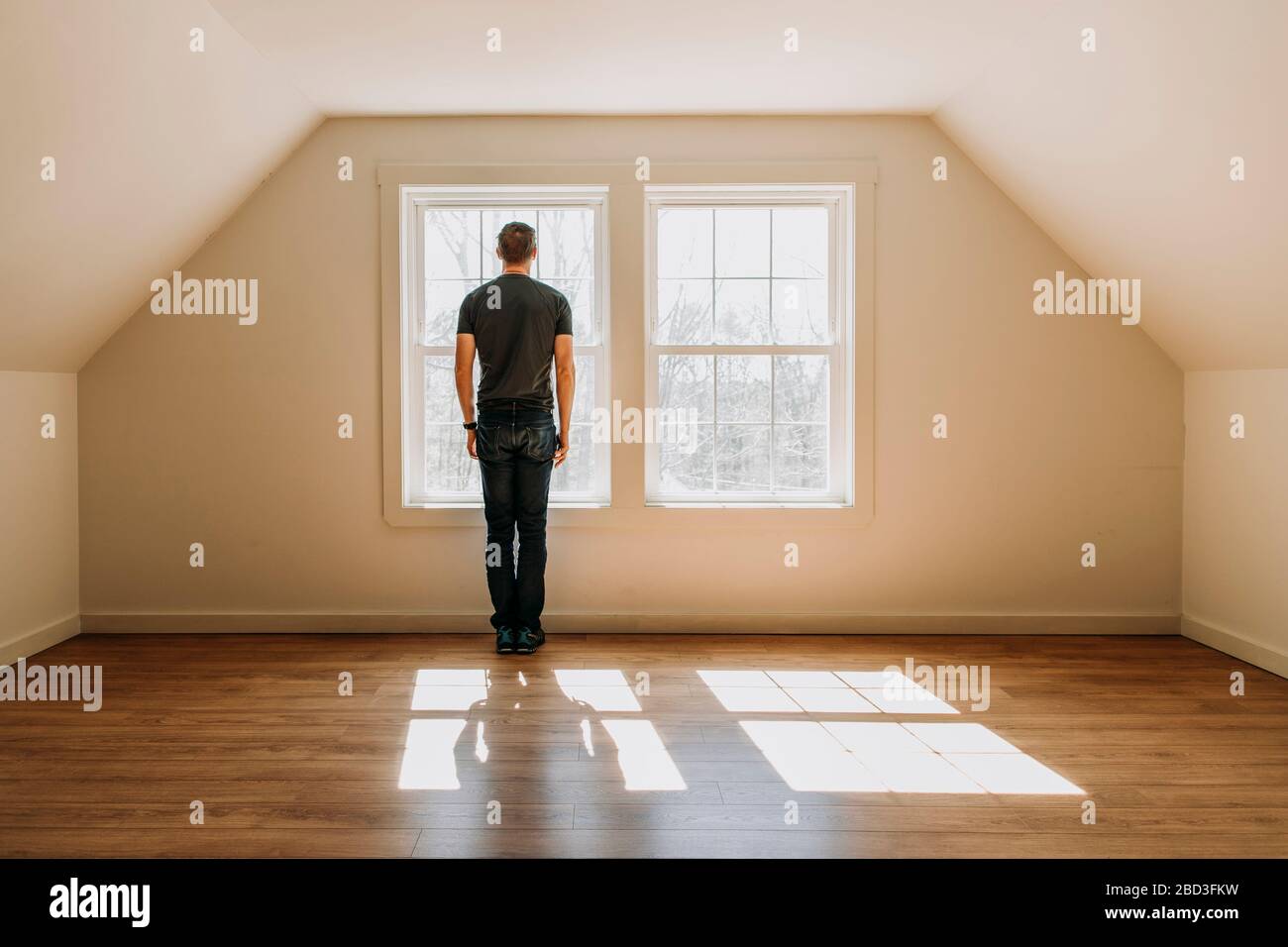 man stands in front of interior window in empty lonely minimalist room Stock Photo