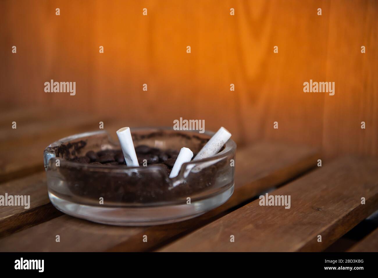 Cigarette in glass ashtray on wooden table. Stock Photo