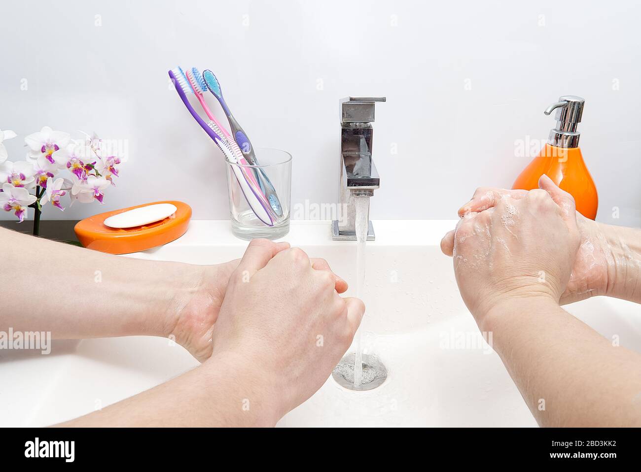 two people wash their hands with soap under running water in white sink ...
