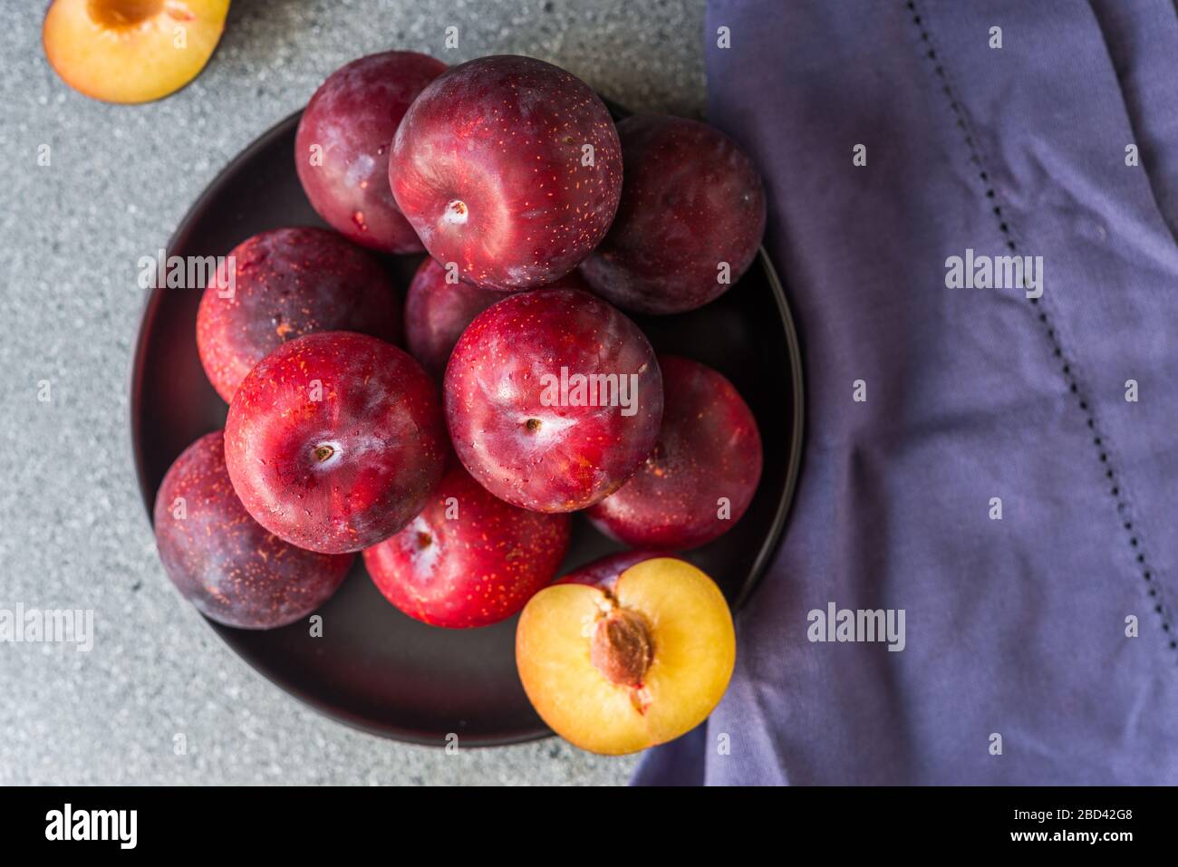 Red organic plums against grey stone background. Stock Photo