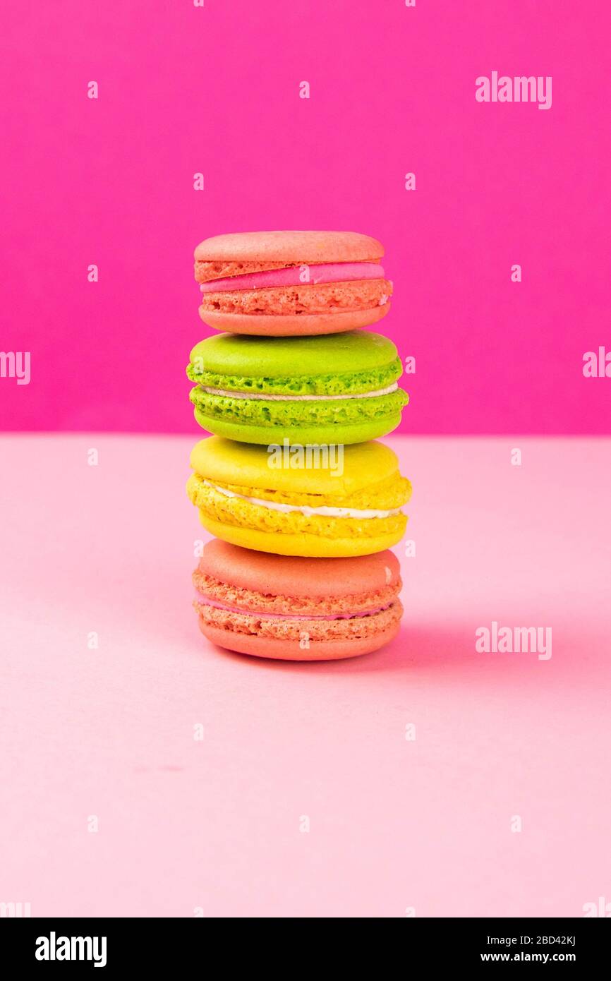 Multi-colored macaroons stand in a pile on a pink table Stock Photo