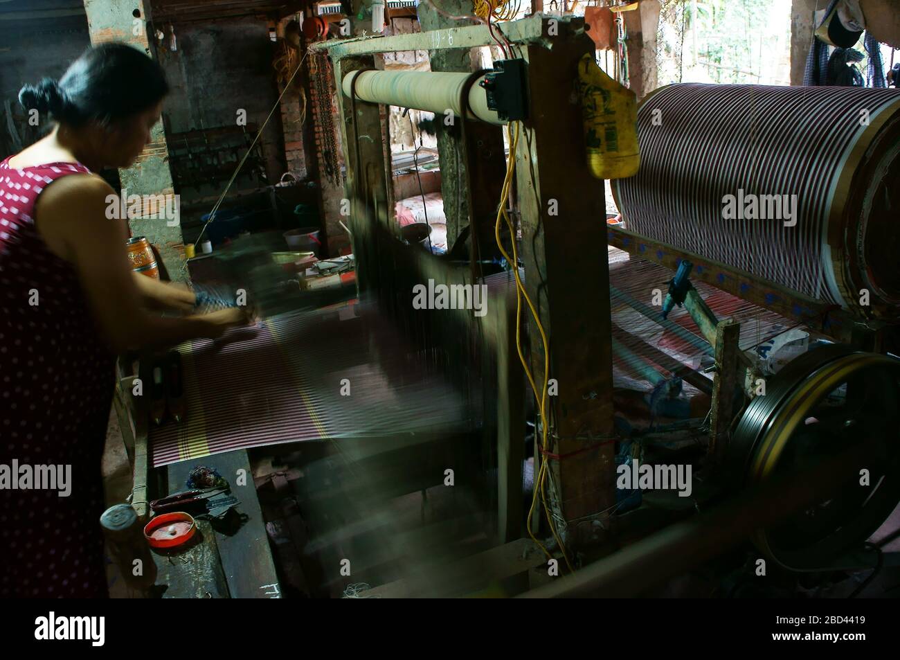 MEKONG DELTA, VIET NAM- NOV 15, 2013: Vietnamese woman standing to work with weaving machine to make scarf from yarn at inside home on day Stock Photo