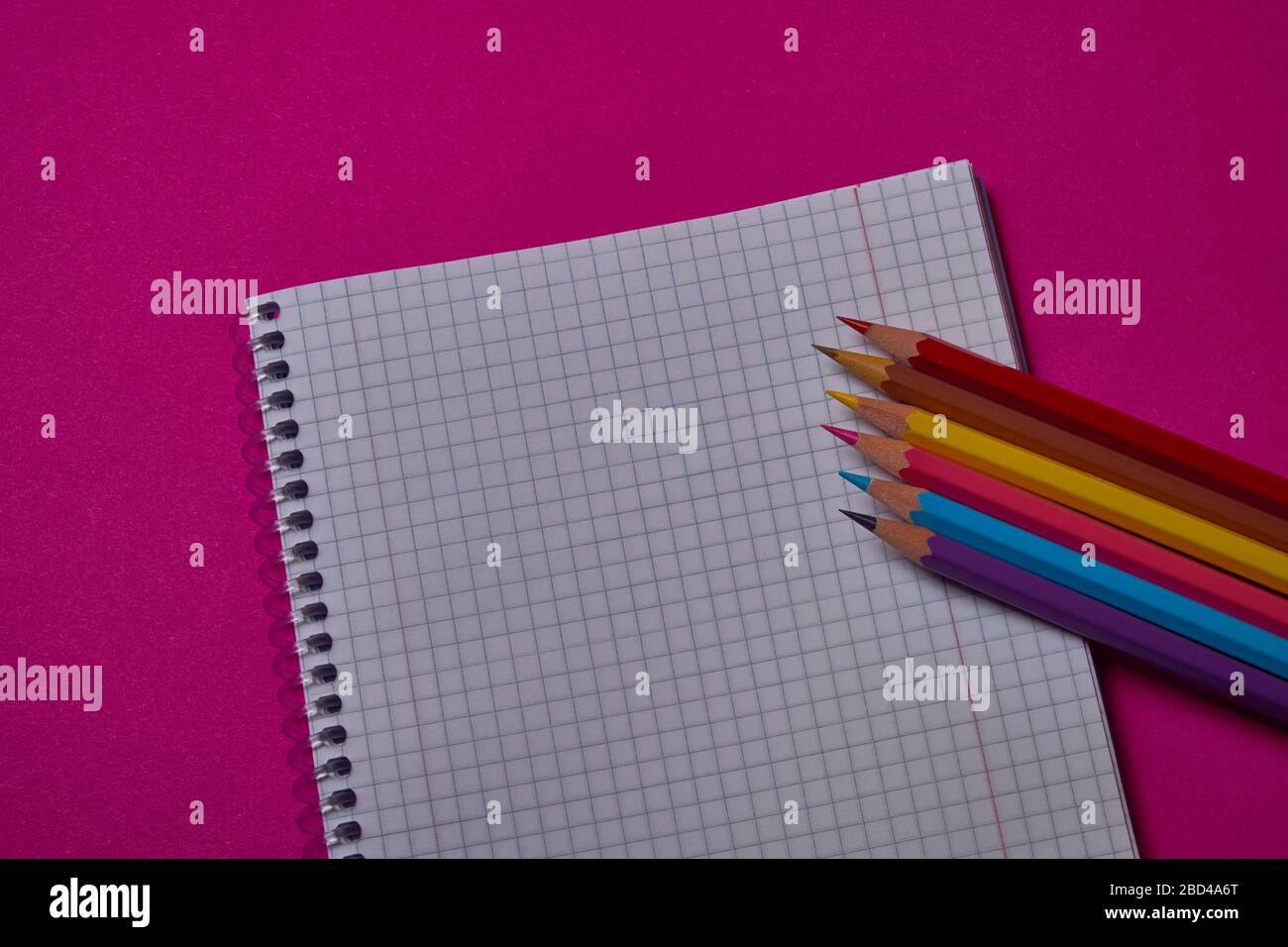 Multi colored crayons and binder notepad at magenta background with copy space. Stock Photo