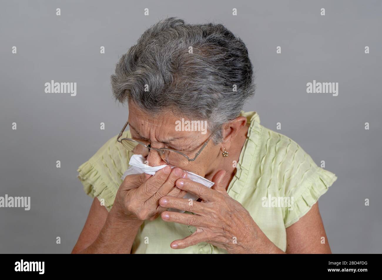An old woman sneezing and covering his mouth and nose Stock Photo