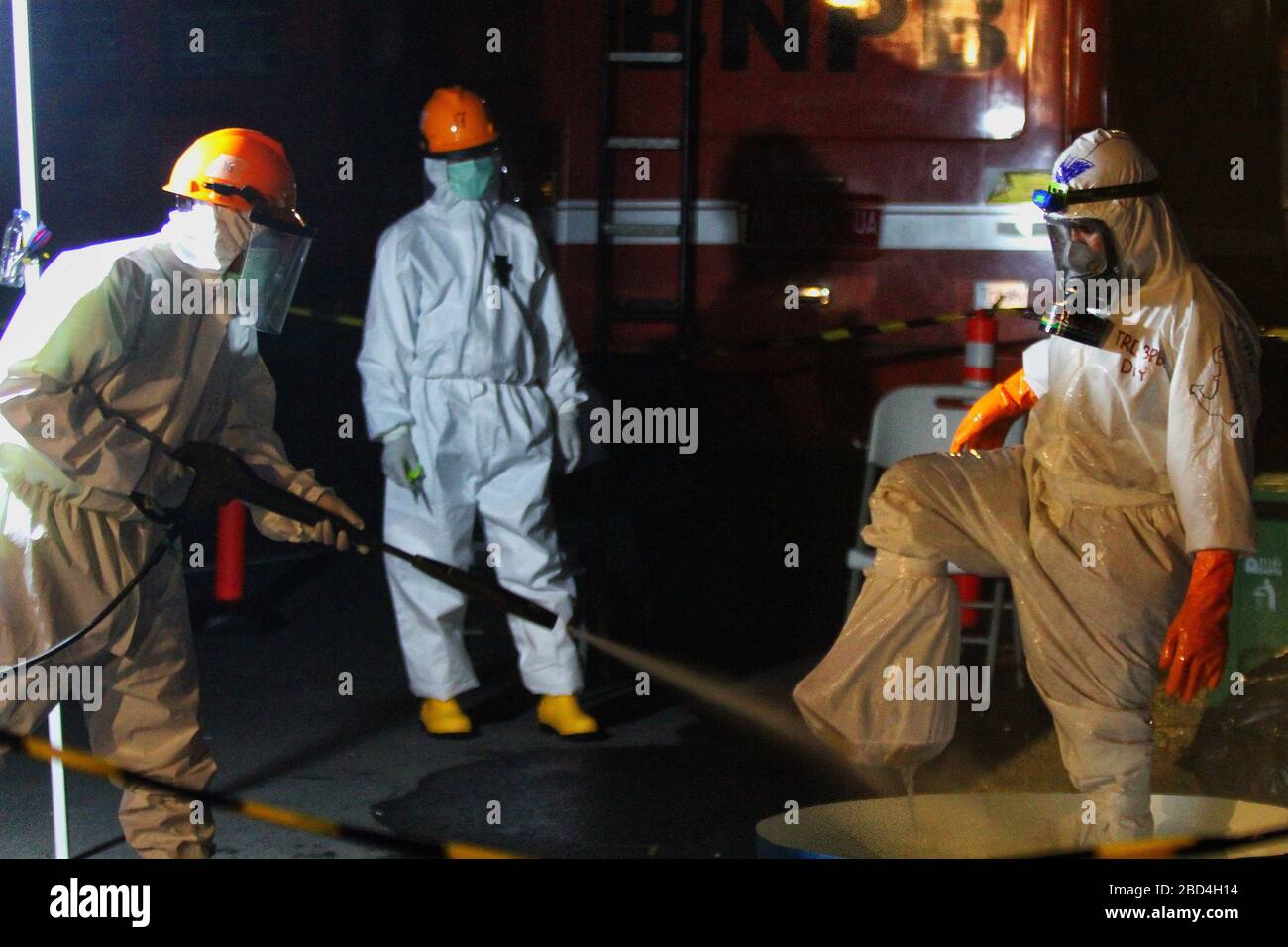 Officers wearing protection suits go through the decontamination area to be sprayed with disinfectant after burying corona virus victims in Yogyakarta, Indonesia, Monday, April 6, 2020. This activity is carried out to clean officers from being contaminated with corona virus or Covid-19. Stock Photo