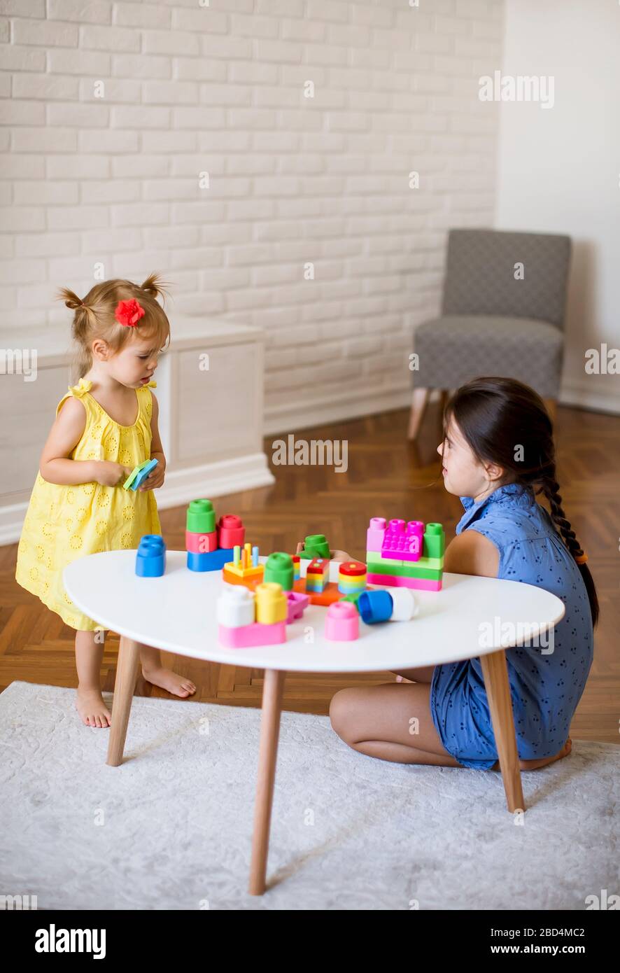 Two cute little girls play with blocks at the table in the room Stock ...