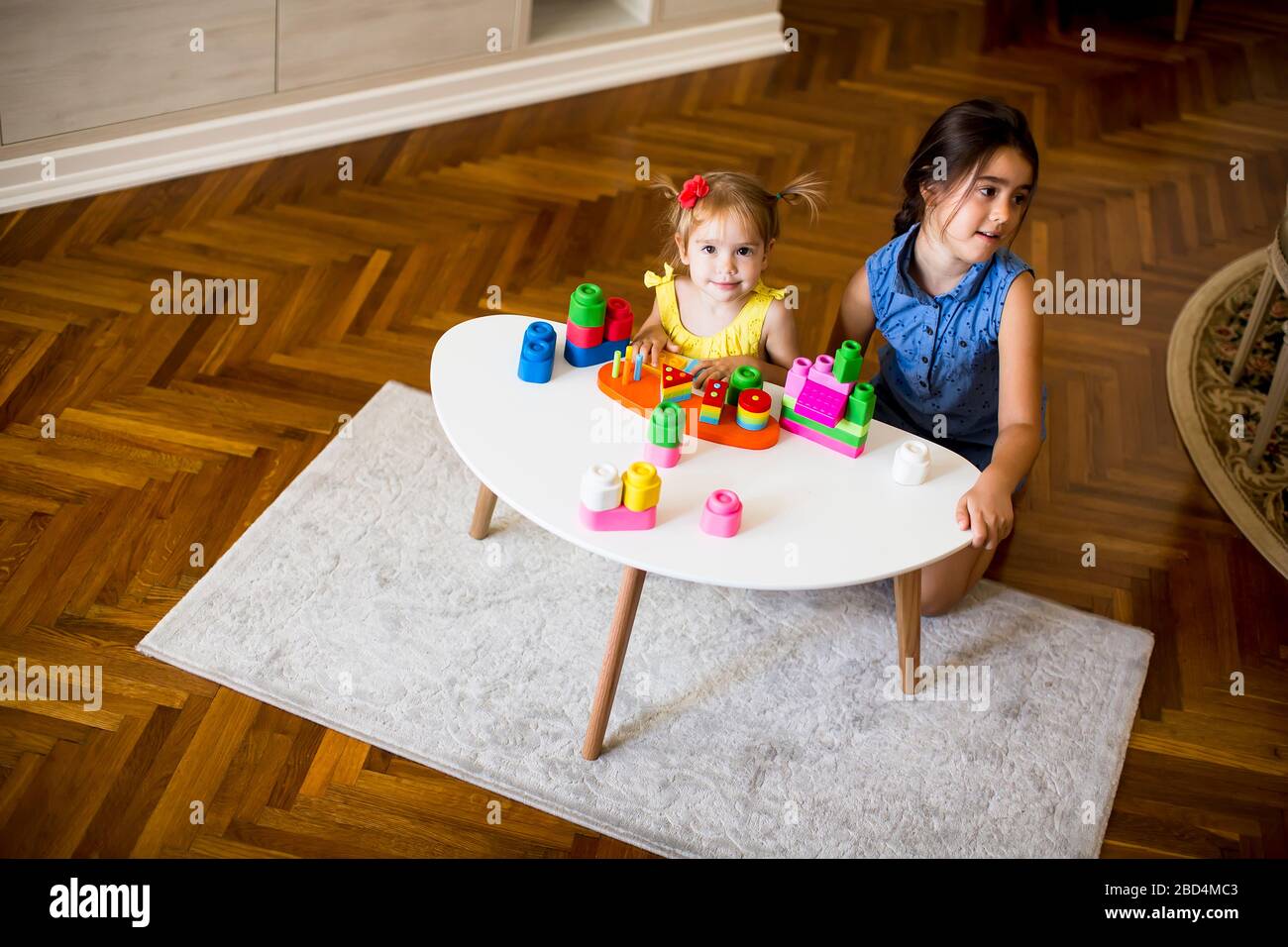 Two cute little girls play with blocks at the table in the room Stock ...